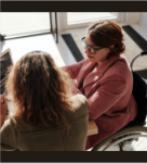 Two women sitting at desk and one is a a wheelchair and they are using the computer